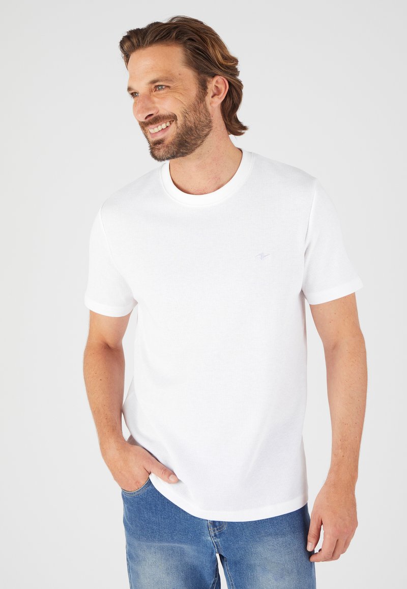 Camiseta blanca de manga corta hecha de algodón texturizado, con cuello redondo y un pequeño logo bordado en el lado izquierdo del pecho.