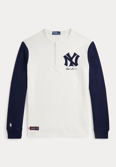 T-shirt à manches longues blanc avec des manches bleu marine, logo des New York Yankees et signature Ralph Lauren sur la poitrine, et petit emblème de cheval sur le poignet.