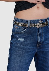Dunkelblaue Jeans aus Denim mit distressierten Details, ausgestattet mit einem silberbesetzten schwarzen Gürtel und einem geraden Schnitt; sichtbare Kontrastnähte.