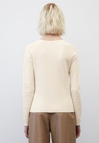 Pull à manches longues de couleur crème avec un motif en maille texturée et un col rond ; associé à un pantalon en tissu marron, lisse.