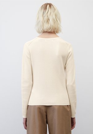 Pull à manches longues de couleur crème avec un motif en maille texturée et un col rond ; associé à un pantalon en tissu marron, lisse.