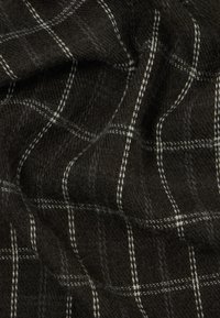 Tissu à motif sombre présentant un design à carreaux en blanc et gris, avec une texture douce et une apparence lâche et drapée.