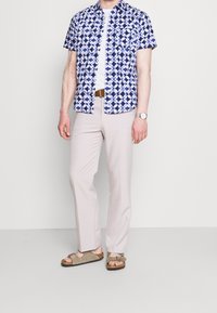 Korte mouwen shirt in een blauw-wit geometrisch patroon, gecombineerd met lichtbeige broek en bruine sandalen. Lichtgewicht stof, comfortabele pasvorm.