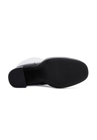 Black leather boot lying on its side showing textured sole and stacked heel on white background.