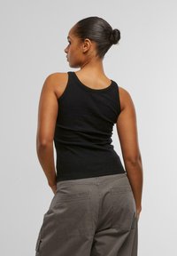 Débardeur en ribbed noir avec un design ajusté, des bords sans couture et un col en scoop, associé à un pantalon cargo vert avec de grandes poches arrière.