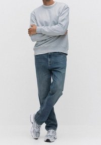 Sweat-shirt gris, jean bleu et baskets grises ; tenue décontractée avec poignets et taille côtelés, texture denim classique et matériaux mixtes.