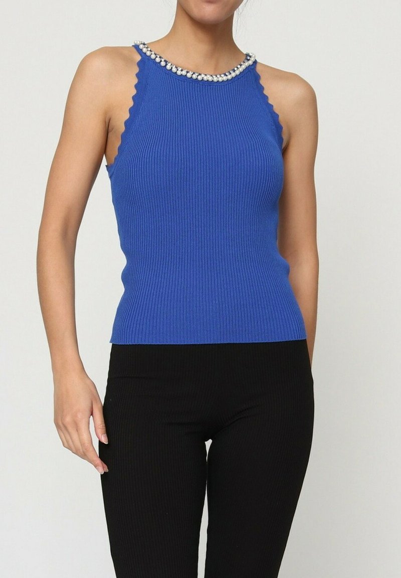 Débardeur bleu côtelé avec des bords festonnés et un décolleté orné. Porté avec un pantalon noir côtelé.