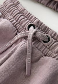 Lyse lilla joggingbukser med tekstureret stof, elastisk talje og snøre. Bemærkelsesværdige sorte hætter fremhæver designet.