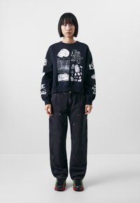 Felpa nera con stampe grafiche bianche, abbinata a pantaloni in denim scuro larghi con tasche laterali, completata da sneakers colorate.