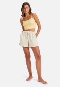 Top court côtelé jaune avec des fines bretelles, associé à un short en lin beige avec une taille élastique et un cordon de serrage.