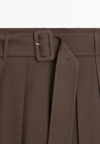 Ceinture en tissu marron avec une boucle rectangulaire recouverte fixée autour d’un pantalon plissé assorti.