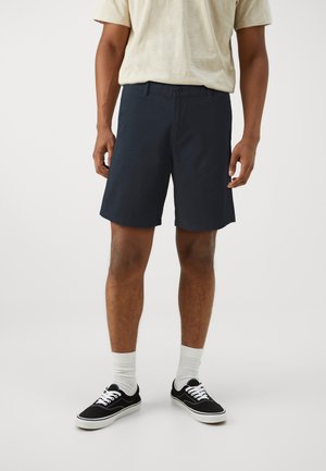 Navy shorts made of lightweight fabric with a flat front, button closure, and side pockets. Paired with black sneakers and white socks.