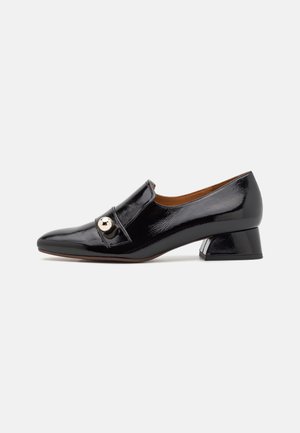 Chaussure en cuir verni noir avec un bout arrondi, une sangle sur le devant ornée d'un accent doré, et un petit talon carré. Texture lisse et design élégant.