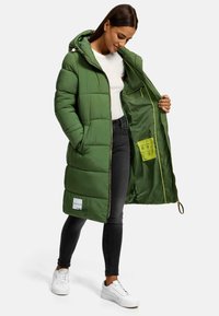 Green puffer coat with a hood, zip front, interior pocket, and contrasting yellow lining. Features a quilted design and logo label.