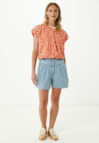 Top corto de manga corta en color naranja con estampado de cebra, combinado con pantalones cortos de mezclilla clara con pliegues. Se lleva con zapatillas metálicas doradas.