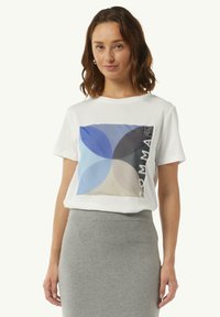 Biała bawełniana koszulka z krótkim rękawem, zdobiona wielokolorowym geometrycznym wzorem w odcieniach niebieskiego i beżowego, z napisem "COMMAS" po prawej stronie.