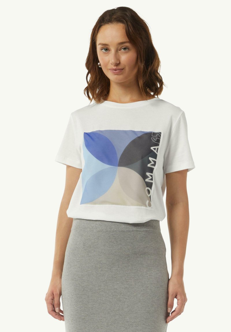 Biała bawełniana koszulka z krótkim rękawem, zdobiona wielokolorowym geometrycznym wzorem w odcieniach niebieskiego i beżowego, z napisem "COMMAS" po prawej stronie.