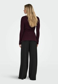 Maglione bordeaux a maglia con corpetto aderente e orlo svasato, abbinato a pantaloni neri a gamba larga. Tessuto morbido, maniche lunghe, dettagli minimali.
