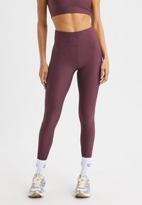 Burgunderfärgade ribbade högmidjade leggings i kombination med en matchande kort topp, som bärs med grå och beige träningsskor samt vita strumpor.