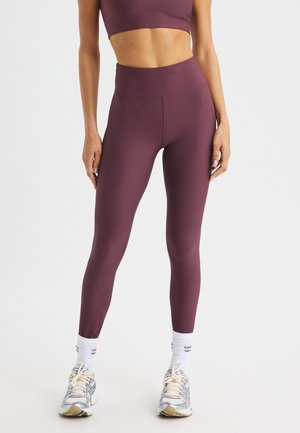 Bordeauxfarbene, gerippte, hochgeschnittene Leggings, kombiniert mit einem passenden Crop-Top, getragen mit grauen und beigen Sportschuhen und weißen Crew-Socken.