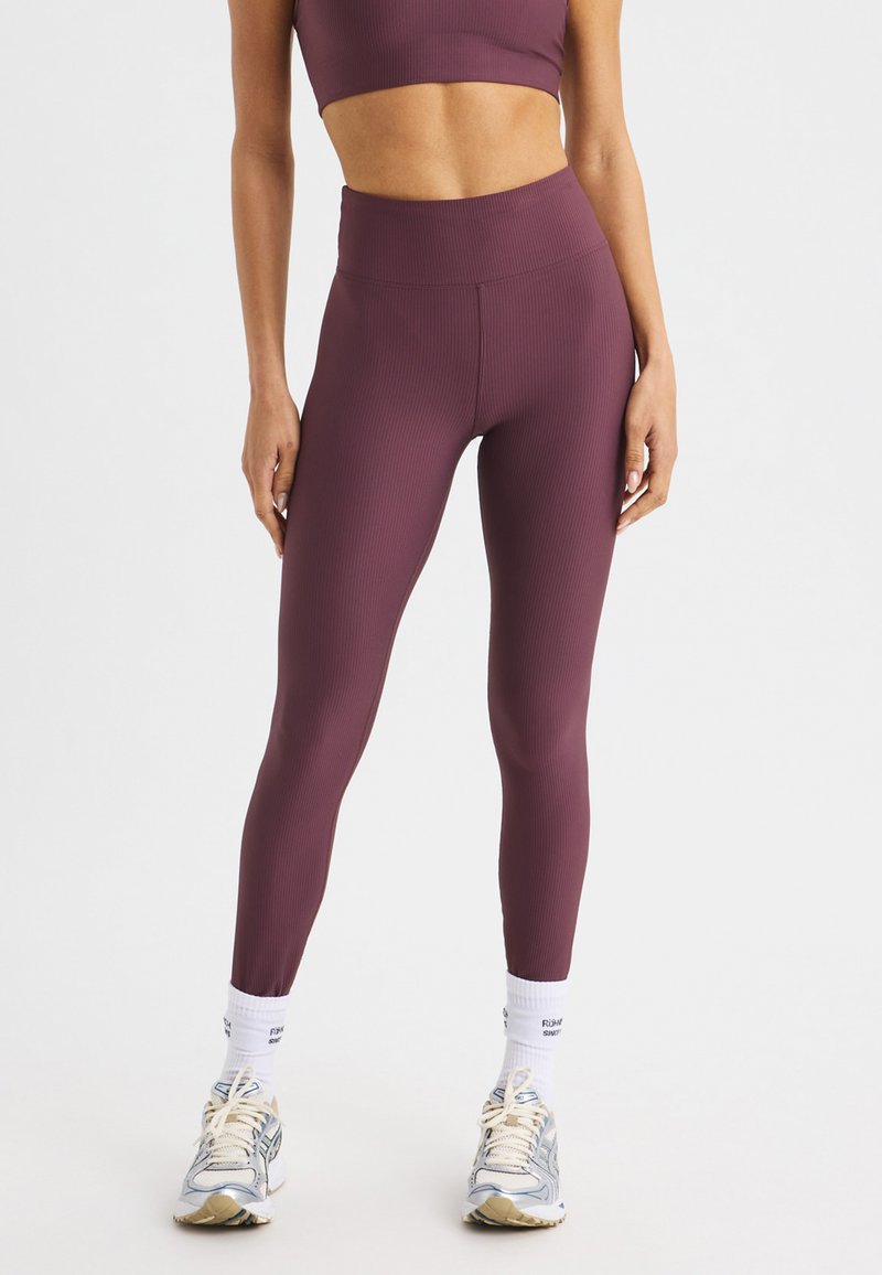 Burgunderfärgade ribbade högmidjade leggings i kombination med en matchande kort topp, som bärs med grå och beige träningsskor samt vita strumpor.