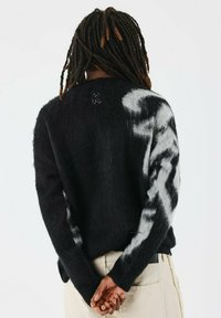 Pull noir avec un motif abstrait blanc, texture douce, manches longues et col rond. Il présente un logo brodé au dos.