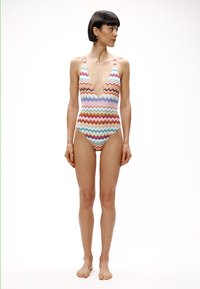 Jednoczęściowy strój kąpielowy z wzorem w zygzaki w pastelowych kolorach. Głęboki dekolt w kształcie litery V, wysokie wycięcia na nogi oraz miękki, teksturowany materiał.