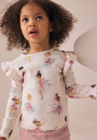 Witte longsleeve met kleurrijke ballerina-patronen, gerimpelde schouderaccenten en een gegolfde zoom; gecombineerd met lichtroze broek.