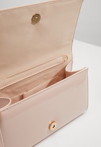 Světle růžová kabelka z lakované kůže se zapínáním na cvok, vnitřní kapsou a přihrádkami na karty, s hladkou texturou a zlatými kovovými doplňky.