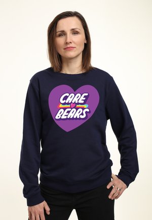 Felpa blu navy con un grande grafico a forma di cuore viola e il testo "CARE BEARS" in bianco, accentuato da linee colorate.
