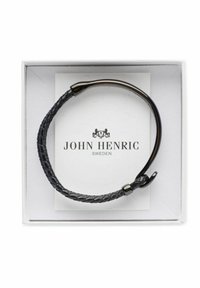 Svart flätad läderarmband med en böjd svart metallspänne, presenterad i en vit låda med "John Henric Sweden"-logotyp.