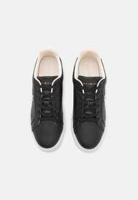 Black leather sneakers with round toe, white rubber sole, and black laces. Features beige accents inside and gold brand logo on tongue.