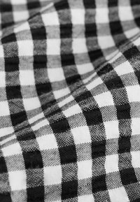 Tissu à carreaux noir et blanc présentant un motif de carrés alternés, avec une texture douce et une apparence légèrement froissée.