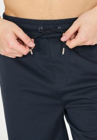 Marinblå sweatpants med texturerad tyg, elastisk midja med dragsko och metallaccenter vid dragskon.
