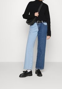 Jeansy w odcieniach niebieskiego i jasnoniebieskiego z luźnym fasonem, zestawione z czarnym prążkowanym swetrem i czarnymi butami, uzupełnione czarną torebką na ramię.