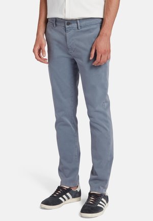 Graue Baumwollchinos mit Slim-Fit-Schnitt, ausgestattet mit einer Fronttasche, Knopfverschluss und einer glatten Textur, kombiniert mit schwarzen Sneakers.