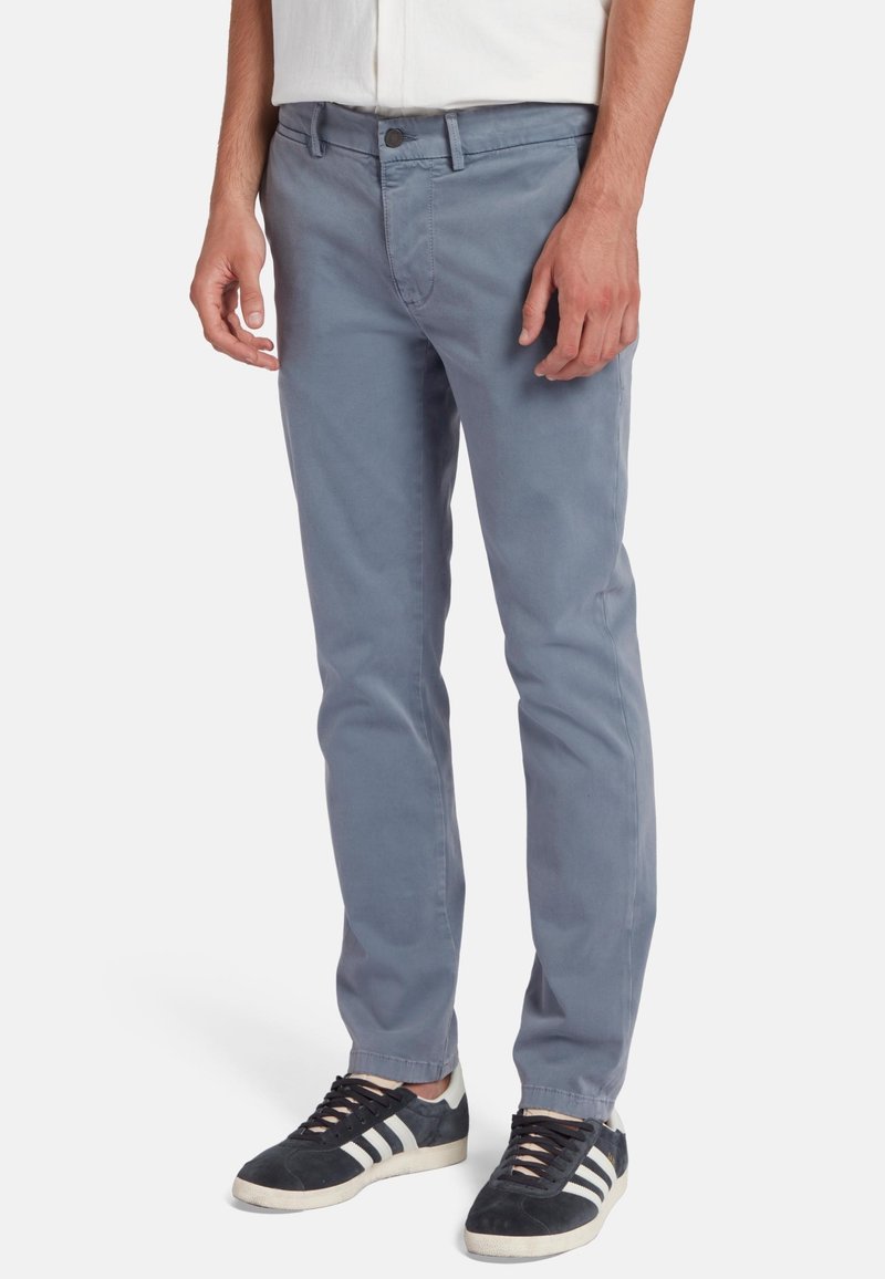 Grijze katoen chino's met een slim fit, voorzien van een voorzak, knoopsluiting en een gladde textuur, gecombineerd met zwarte sneakers.