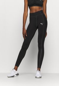 Czarne legginsy sportowe z wysokim stanem, z kontrastowym białym przeszyciem i małym białym logo na lewej udzie. Gładka tekstura.