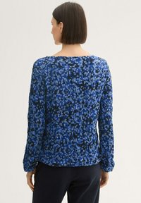 Langärmlige Bluse mit einem abstrakten blau-schwarzen Muster, ausgestattet mit einem weit geschnittenen Halsausschnitt und strukturiertem Stoff.