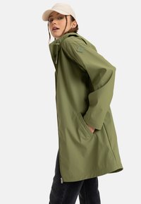Olive green water-resistant jacket with a zip closure, hood, and two side pockets; smooth texture and relaxed fit.