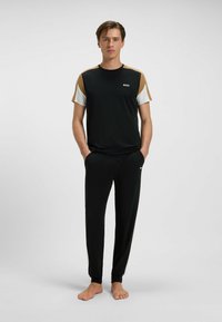 Czarny zestaw odzieży sportowej składający się z koszulki z krótkim rękawem z beżowymi i białymi akcentami, w połączeniu z czarnymi zwężającymi się spodniami. Miękki, gładki materiał.