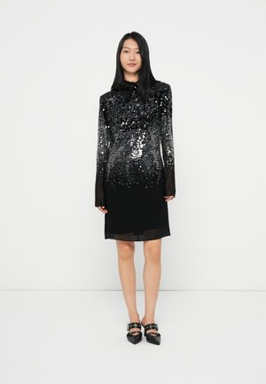 Black dress featuring an ombre effect with silver sequins, long sleeves, and a high neckline. Paired with pointed-toe black shoes.