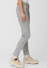Světlé šedé slim-fit džíny s pěti kapsami, poutky na opasek a hnědou koženou visačkou na zadní straně. V páru s robustními béžovými turistickými botami.