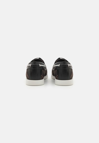 Zapatos de charol negro y marrón con suelas blancas, que presentan herrajes de cordones en los laterales y una superficie de cuero suave.