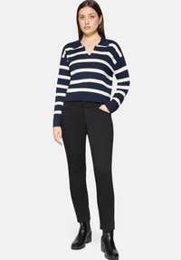 Pull-over à rayures bleu marine et blanches avec col et encolure en V, associé à un pantalon noir slim et des bottines noires. Texture lisse.