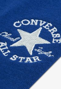 Το μπλε ύφασμα διαθέτει λευκό κεντημένο κείμενο που γράφει «CONVERSE» πάνω από ένα αστέρι και «ALL STAR» από κάτω, με διακριτή υφή στο υλικό.