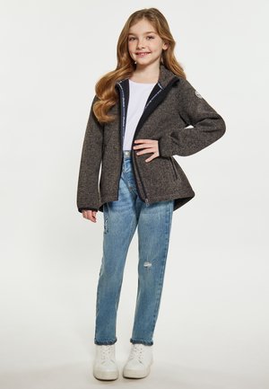 Giacca grigia con zip e bordi neri, realizzata in tessuto morbido. Indossata sopra una maglietta bianca e abbinata a jeans chiari strappati e sneakers bianche.