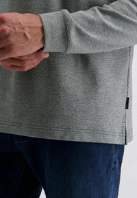 Langärmliges Hemd in Hellgrau mit strukturiertem Muster, ausgestattet mit einem seitlichen Schlitz und kontrastierenden Nähten, kombiniert mit dunkler Denim.