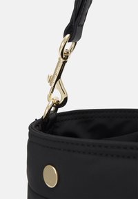 Borsa in nylon nera con un dettaglio di chiusura in metallo dorato e bottone, dalla texture liscia e dalla forma morbida e arrotondata.