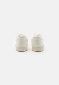 Weiße Sneakers mit glattem synthetischem Obermaterial, gepolstertem Schaft und strukturiertem beige Gummisohle. Minimalistisches Design ohne sichtbare Markenkennzeichnung.